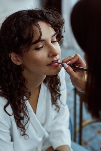 Hand of female makeup artist applying lipstick or gloss on lips of bride