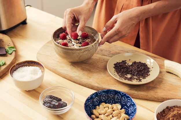 Hand of female putting fresh ripe rasberries on top of smoothie