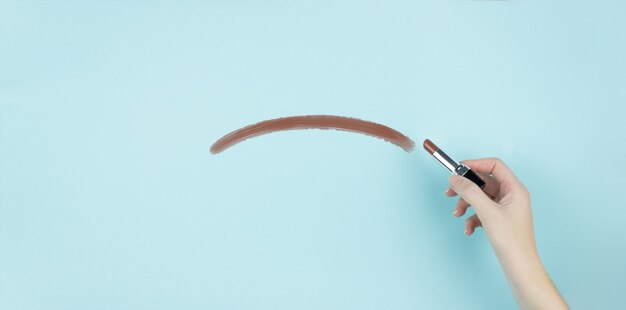 Hand of female writing negative smile with brown lipstick on blue background.