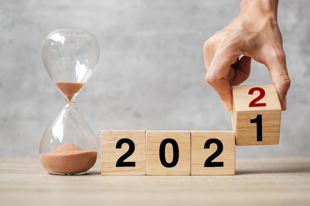 Hand flipping block 2021 tot 2022 tekst met zandloper op tafel. Resolutie, tijd, plan, doel, motivatie, opnieuw opstarten, aftellen en nieuwjaarsvakantieconcepten