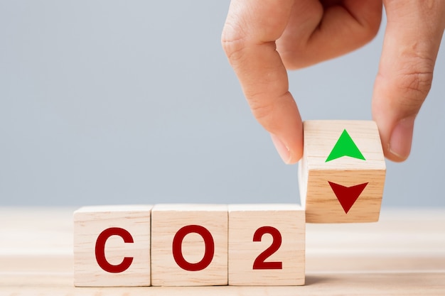 Hand flipping houten kubusblokken naar omhoog en omlaag pijlsymbool met co2 (kooldioxide) tekst op tabelachtergrond. concepten voor gratis koolstof, alternatieve energie en wereldwijde klimaatverandering