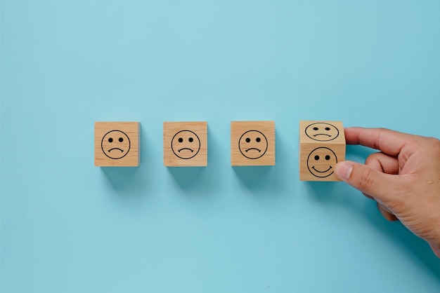 Hand flipping houten kubussen blokken met ongelukkig en blij gezicht pictogram op blauwe achtergrond