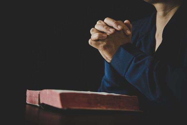 Hand folded in prayer to god on holy bible book in church\
concept for faith spirituality and religion woman person praying on\
holy bible in morning christian catholic woman hand with bible\
worship