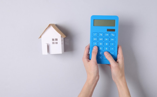 Hand gebruikt rekenmachine op een grijze achtergrond met een huis Berekening van de kosten van huisvesting huur