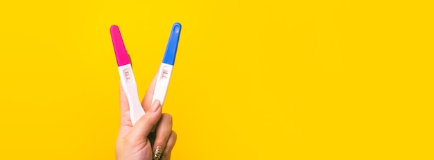 勝利またはピースサインの手のジェスチャーVサイン、黄色の背景に陽性の妊娠検査