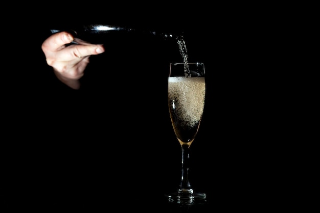 Hand giet champagne in een glas op een zwarte achtergrond