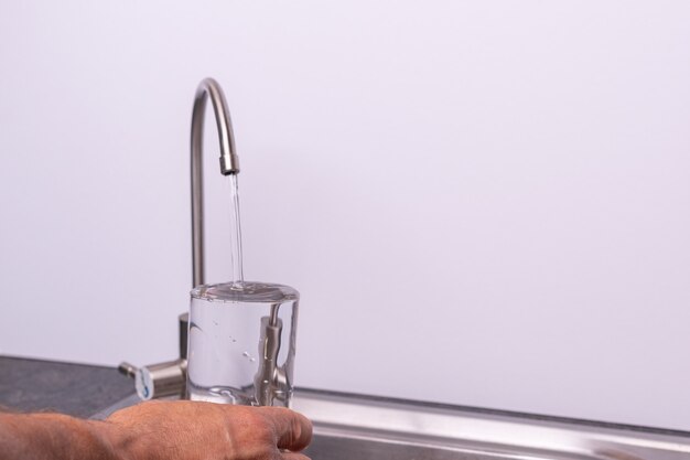 Hand gieten van een glas water uit de filterkraan, witte muur, kopie ruimte