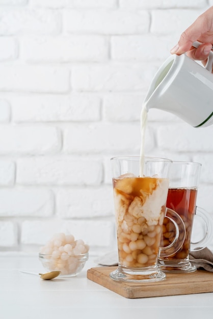 Hand gietende melk in glas met ijsbubbelthee witte bakstenen muur achtergrond