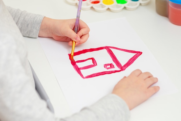 Hand of a girl drawing a red house.