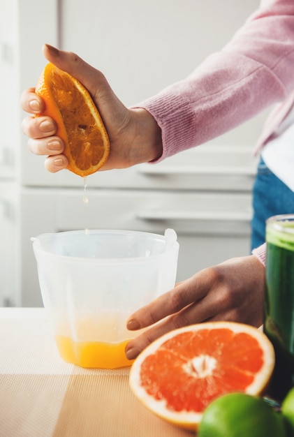 Foto mano della ragazza che spreme un'arancia e produce succhi di frutta fresca a casa