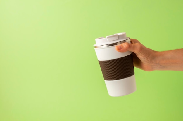 Photo hand of a girl taking a thermos of coffee on a green background copy space