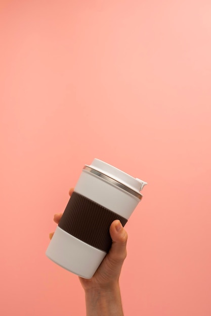 Photo hand of a girl taking a thermos of coffee on a pink background copy space