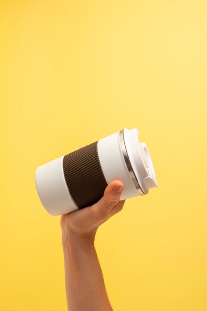 Photo hand of a girl taking a thermos of coffee on a yellow background copy space