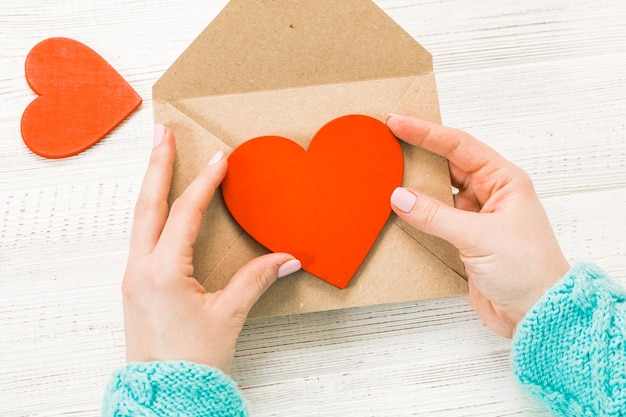 Hand of girl writing love letter on Saint Valentines Day Handmade postcard with red heart shaped figure 14 February holiday celebration Valentine day concept with copy space