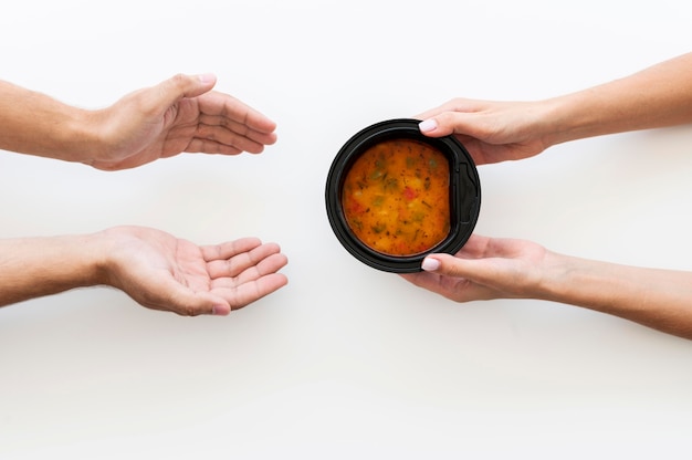 Hand giving bowl of soup to needy person