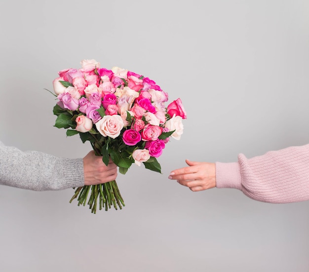 Hand giving reses flowers bouquet to woman on grey background Valentines or mothers day consept