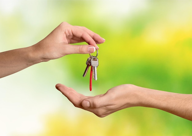 Hand giving set of house keys on light green background