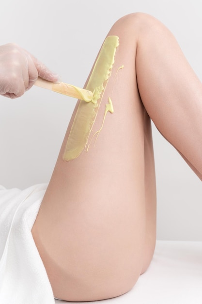 Hand in glove applying green hot wax on slim woman leg using spatula Depilation procedure