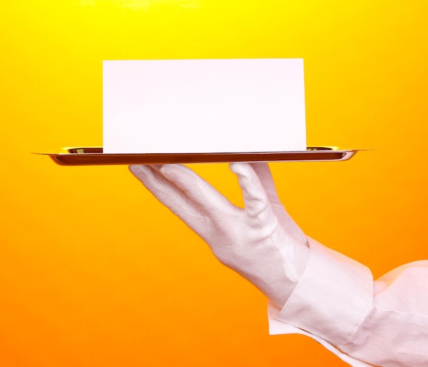 Photo hand in glove holding silver tray with blank card on yellow background