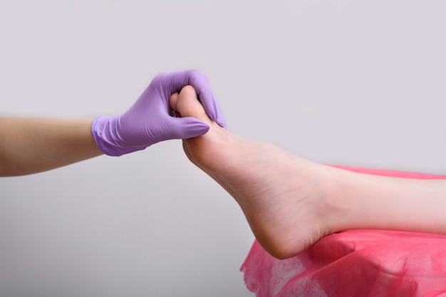 Рука в перчатке держит женскую ногу после педикюра. Салон красоты