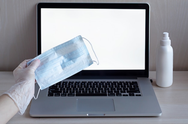 Hand in glove holds a mask on a laptop.