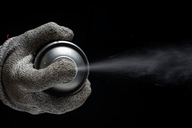 hand in a glove holds a spray can on a black background. .