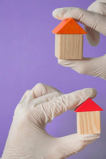 Foto la mano in un guanto tiene una casa di legno - concetto di assicurazione sanitaria o banner medico di famiglia, copia spezie