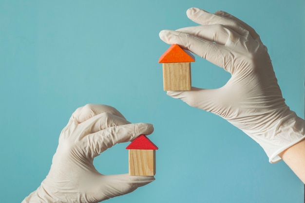 Foto la mano in un guanto tiene una casa di legno - concetto di assicurazione sanitaria o medico di famiglia