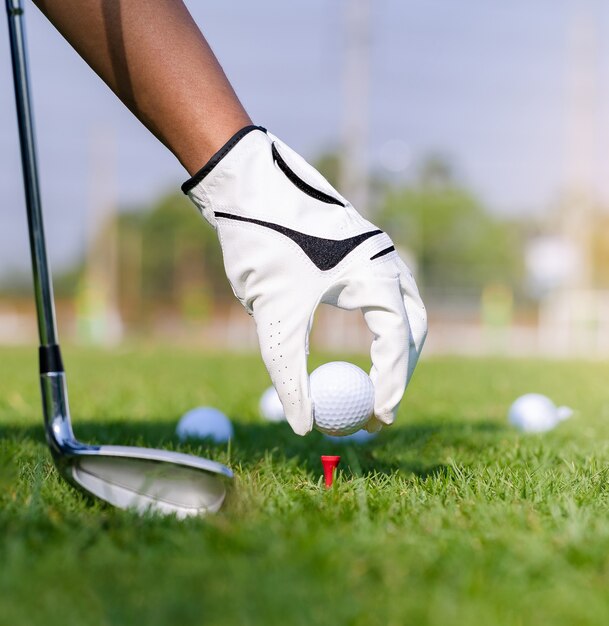 Hand in glove placing golf ball on tee in course