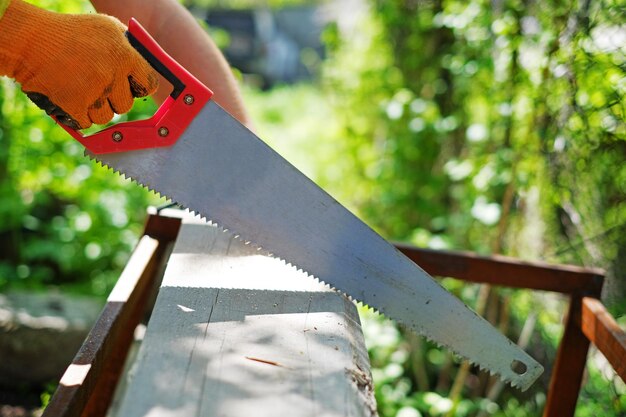 Hand in a glove sawing wooden plank summer background