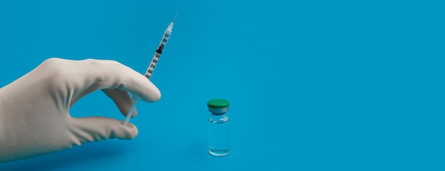 Hand in a glove with a syringe and ampoule on a blue panorama background