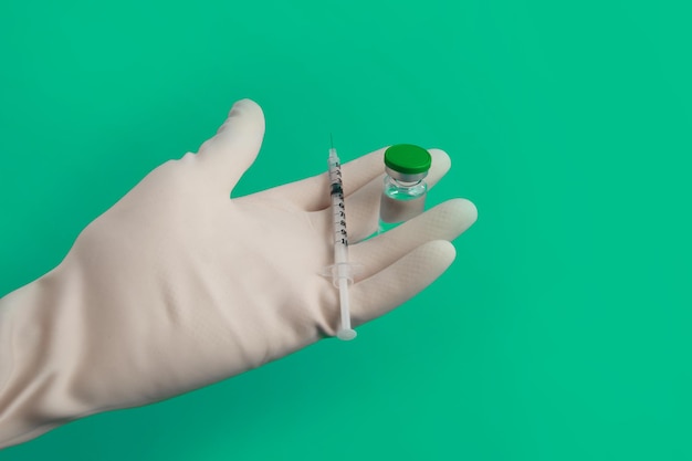 Hand in a glove with a syringe and ampoule on a green background