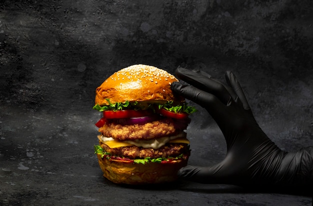 Hand grabbing a big double chicken burger with cheese and vegetables