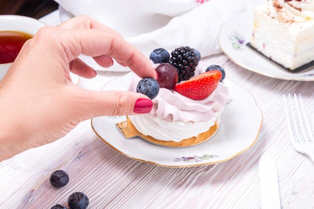 Hand grabbing piece of berry cake decorated with fresh berries on wooden white background