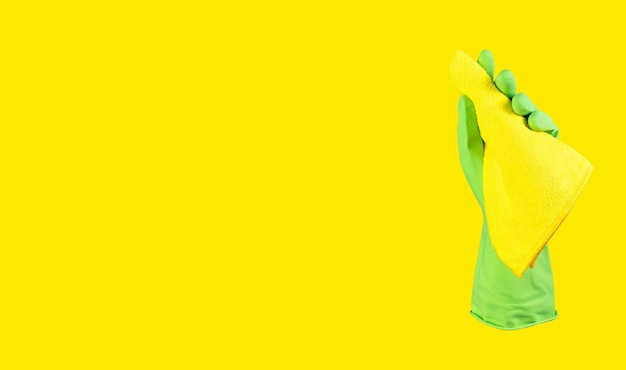 Hand in green glove holding microfiber cloth for wiping dust Yellow banner background with copy space for text