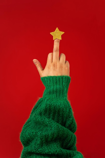 Photo hand in green sweater middle finger with star raised up abstract symbol of christmas tree