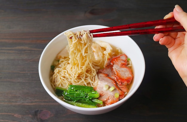 Hand gripping delectable chinese roasted pork egg noodles with\
chopsticks