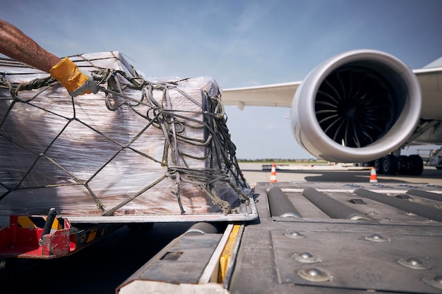 Foto mano dell'equipaggio di terra durante lo scarico dei container di carico dell'aereo di merci contro il motore a reazione dell'aeromobile