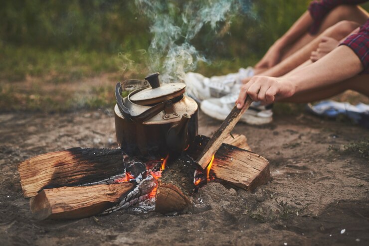 Photo the hand of a guy fixes a fire with a stick on which the kettle is boiling