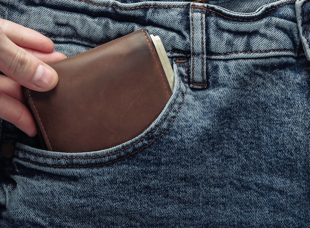 Hand haalt een portemonnee met geld uit de voorzak van een spijkerbroek