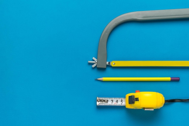 Hand hacksaw tape measure and pencil on a blue background a set
of tools minimal concept of a hand tool flat lay