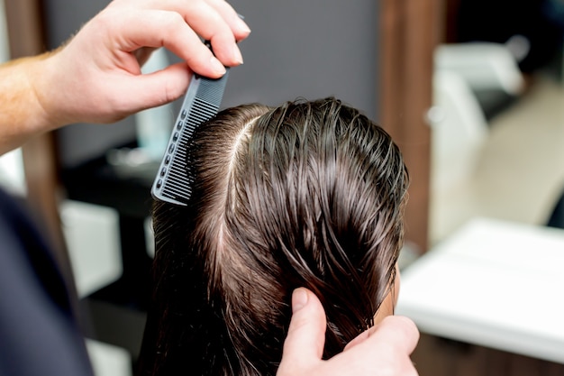 Hand of hairdresser combs wet hair of woman close up.