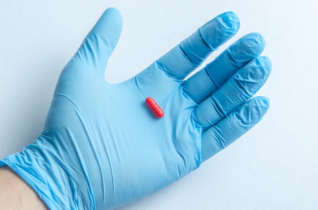 The hand of health care worker in blue medical gloves holding a pill