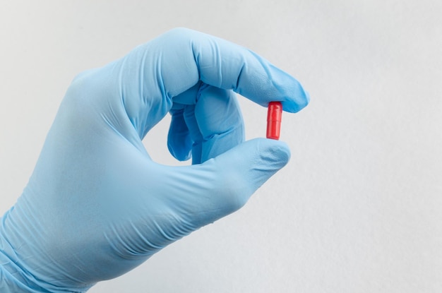The hand of health care worker in blue medical gloves holding a pill