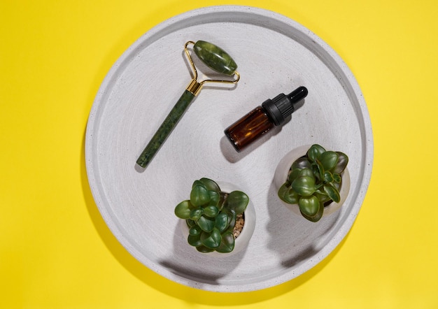 Hand held face massager and brown glass bottle with pipette on round plate