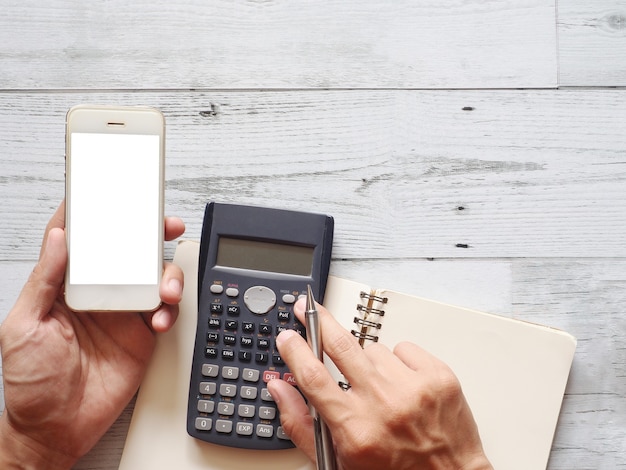 Фото Рука держит мобильный телефон белый экран с помощью калькулятора с ручкой кактуса на столе вид сверху бизнес-концепция
