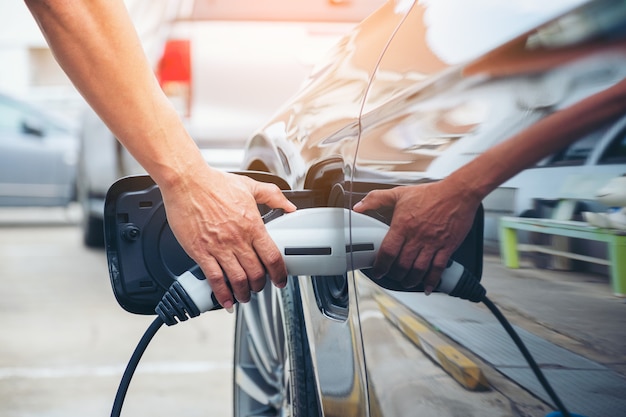 Hand hold of charging modern electric car battery on the street which are the future of the Automobile, Close up of power supply plugged into an electric car being charged for hybrid 