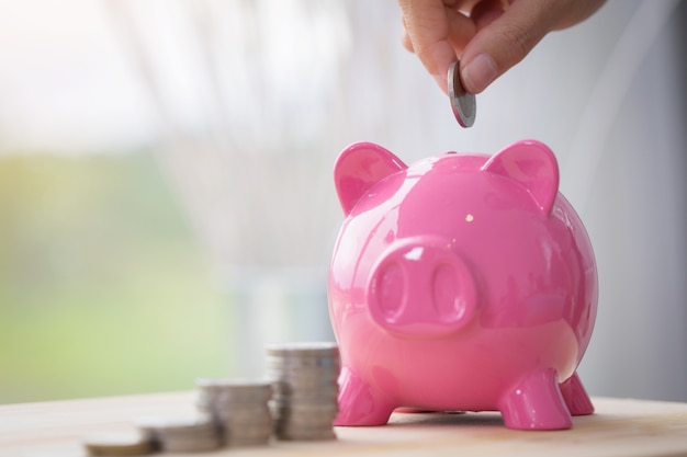 Hand hold coin and saving money in pink piggy bank .