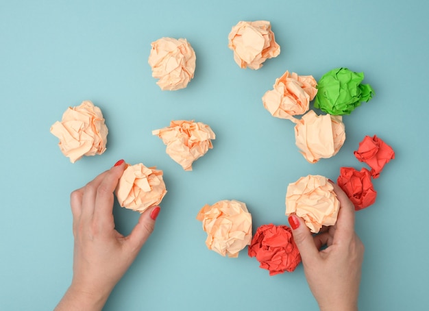 Hand hold crumpled sheets of colored paper on a blue surface. Solution concept, brainstorming, opposition and confrontation, mediator in resolving the issue