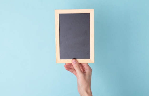 Hand hold empty chalk board on blue background Copy space